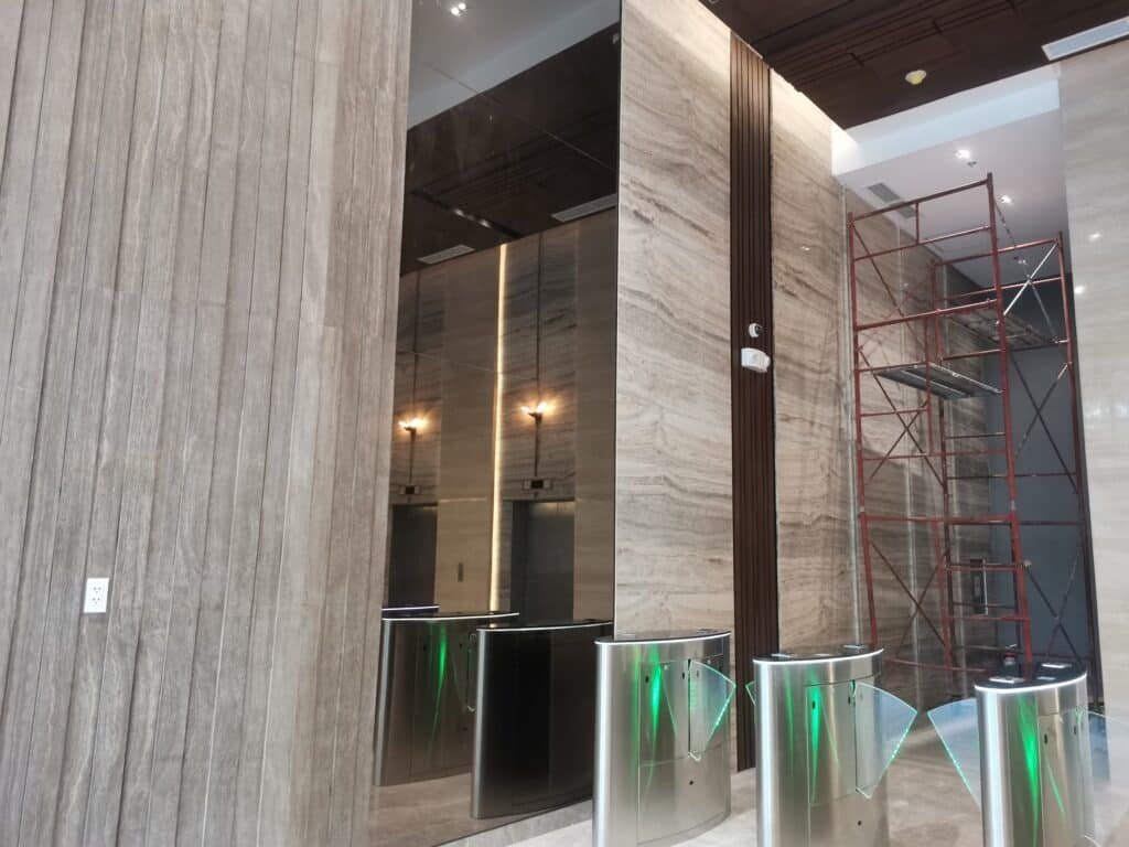 A modern building lobby with turnstiles, mirrored elevator doors, marble walls, and a red scaffolding structure on the right side.