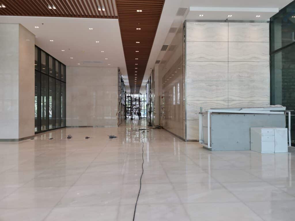 Spacious unfinished modern lobby with marble floors, glass walls, a counter on the right, and construction materials scattered throughout.