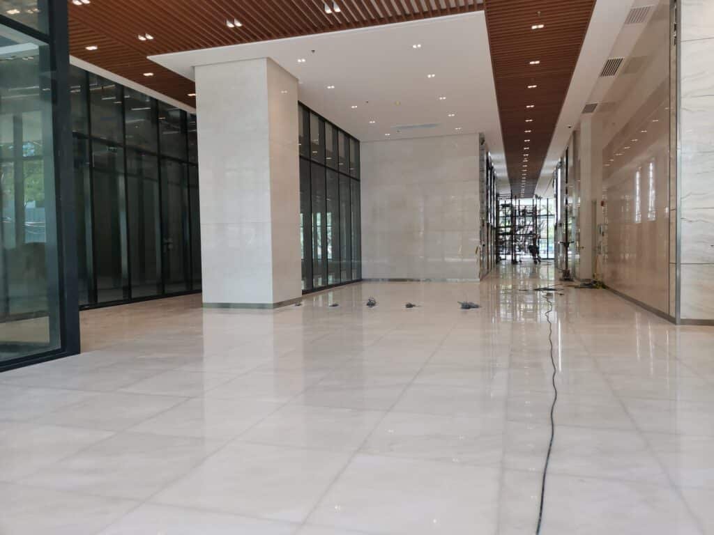 A spacious, modern building lobby with marble floors and glass walls, under bright ceiling lights. Some construction equipment and wires are visible.