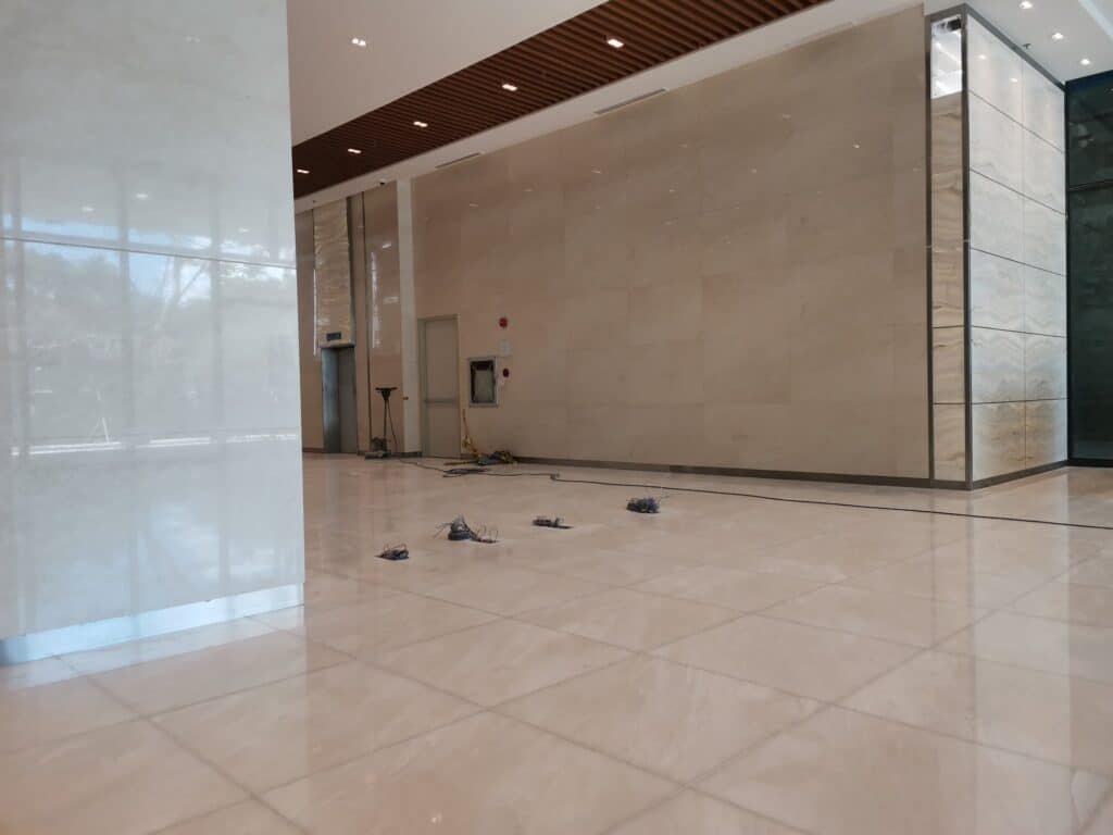 Spacious, empty lobby with beige marble floors and walls; wires and tools are scattered on the floor near the back wall.