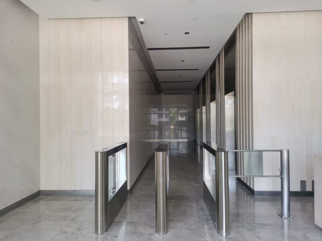 A modern building entrance with glass turnstiles, marble floors, and beige walls, leading to a hallway with reflective surfaces.