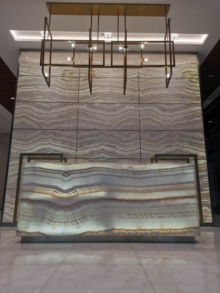 Modern reception desk with backlit onyx surface, set against a wall with matching stone panels and a rectangular brass light fixture above.