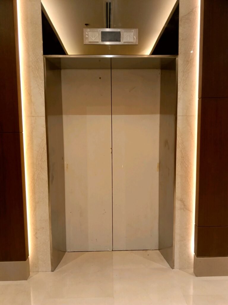 Closed elevator doors in a modern building interior with marble walls and soft lighting.