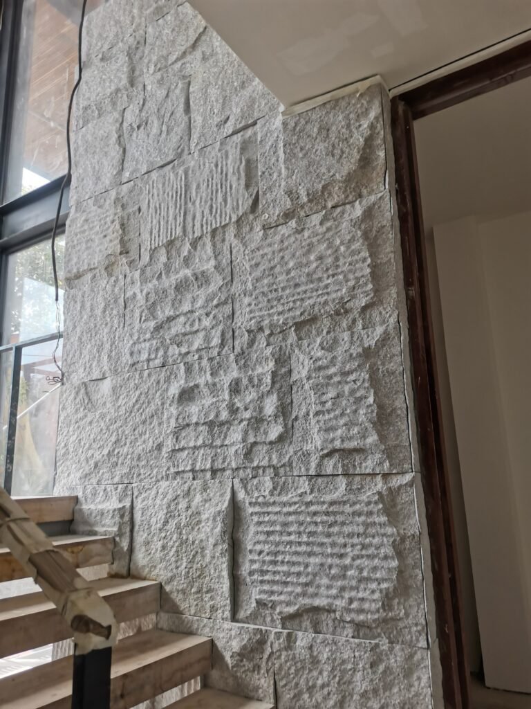 A stone accent wall with rough, textured rectangular blocks next to a staircase under construction inside a building.
