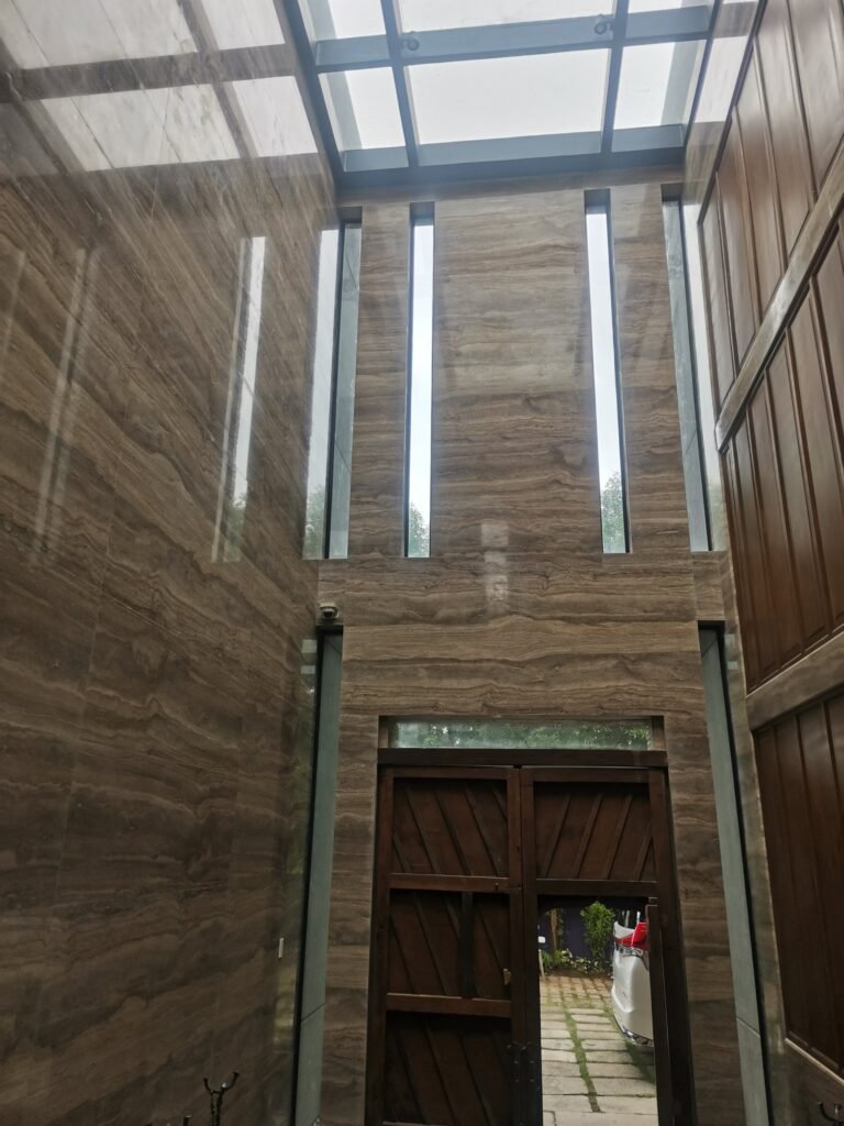 Tall entryway with marble-patterned walls, vertical windows, a wooden door, and a glass ceiling; a white car is parked outside.