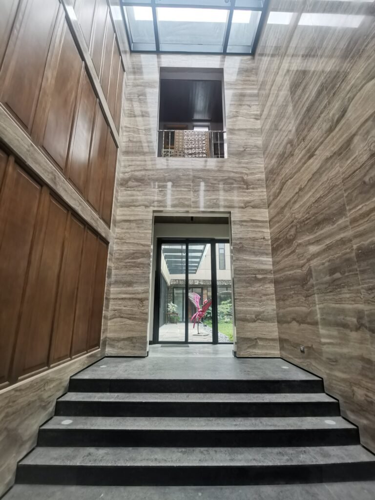 A modern interior features marble walls, a stairway leading to glass doors, and a window above the entrance, with a courtyard and red sculpture visible outside.