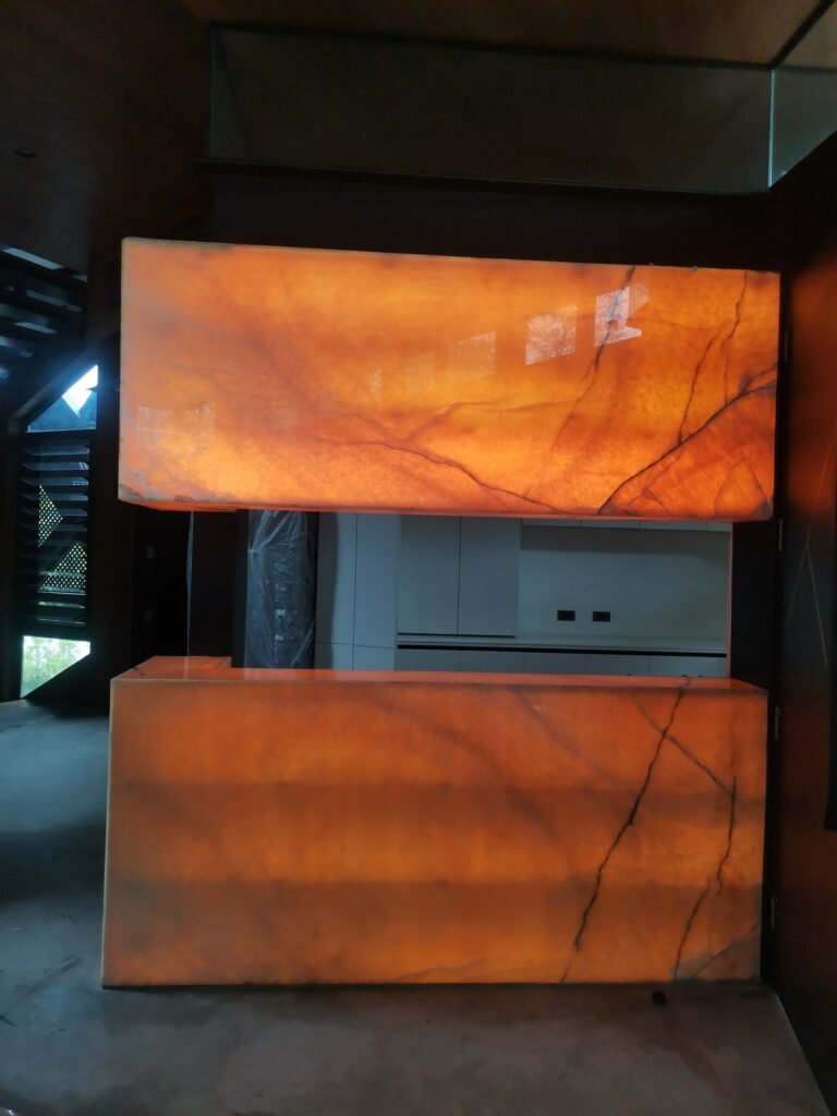 A kitchen area featuring two illuminated, translucent orange stone panels with dark veining, one positioned above the other, partially obscuring the view of white cabinetry behind.